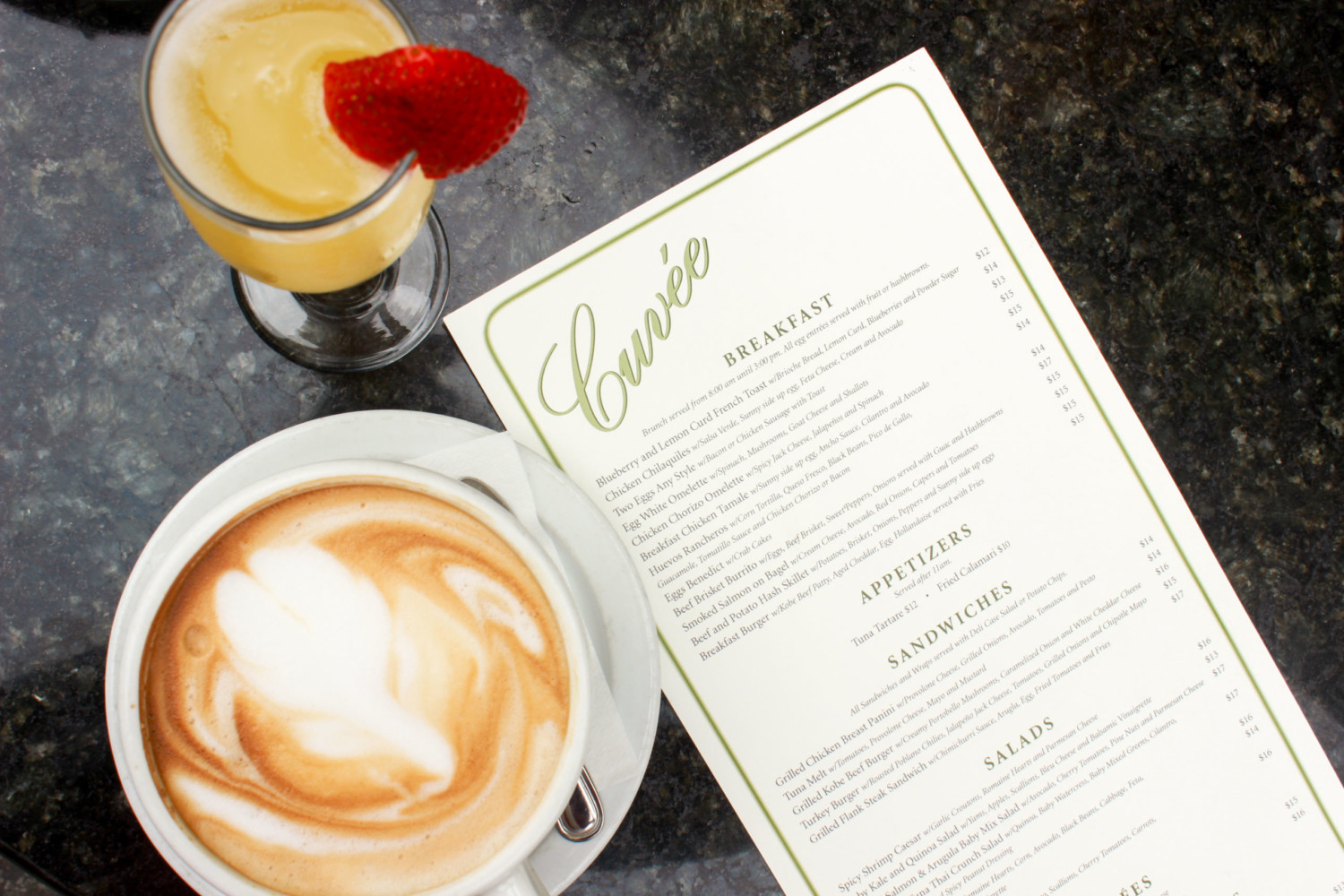 A photo featuring the Cuvee Menu, beside it is a fruit drink and a cup of coffee.