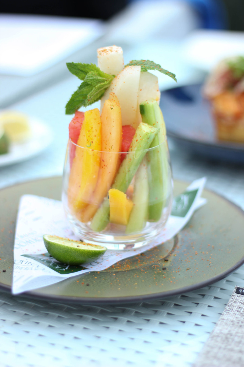 A clear cup with pieces of fruit topped with mint, there is a slice of lime beside it.