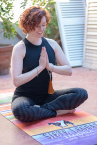 A woman doing yoga. She is sitting cross legged on a yoga mat, her arms folded in front of her chest.