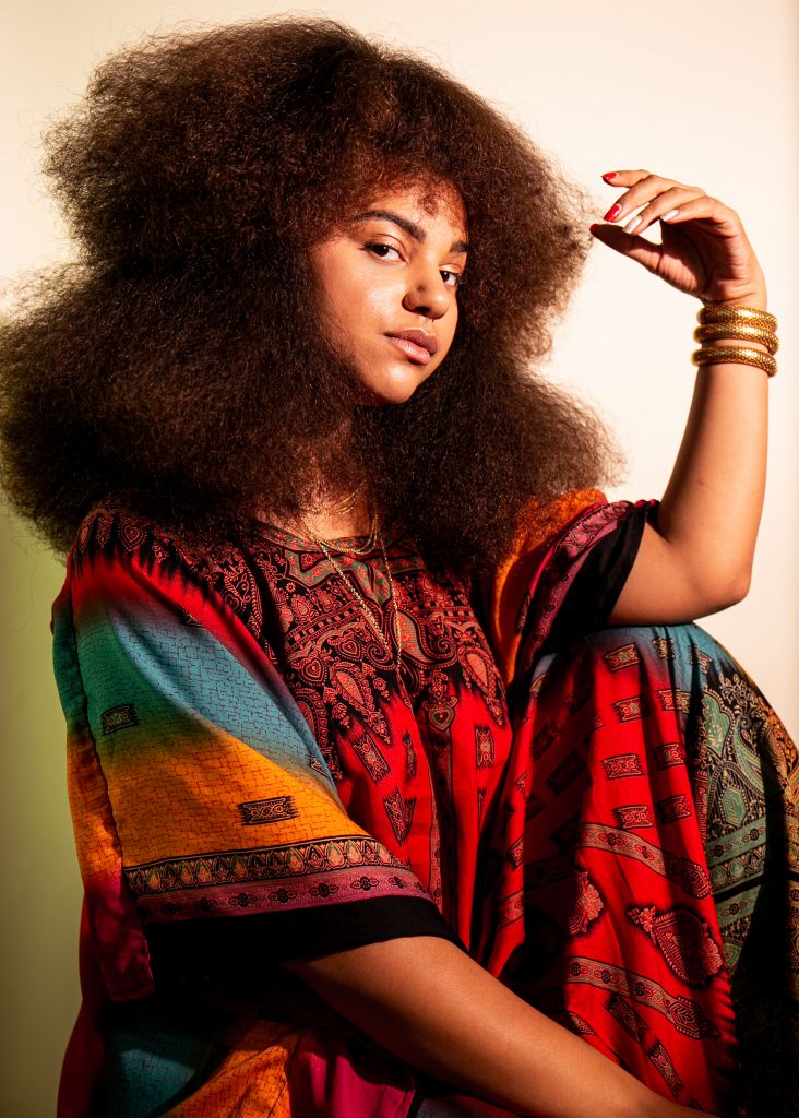 A young woman dressed in colorful garments, she has three bracelets on one arm.