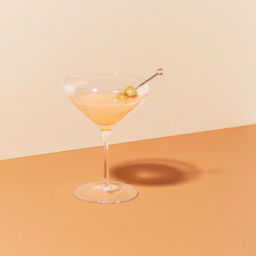 A martini with olives on an orange background