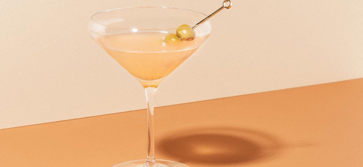 A martini with olives on an orange background