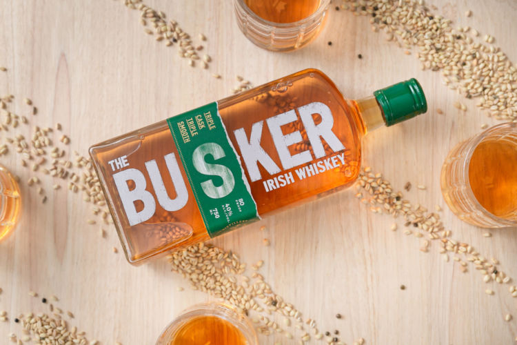 The Busker Whiskey photographed with a two clear glasses and seeds lined up diagonally on a with a wooden background.
