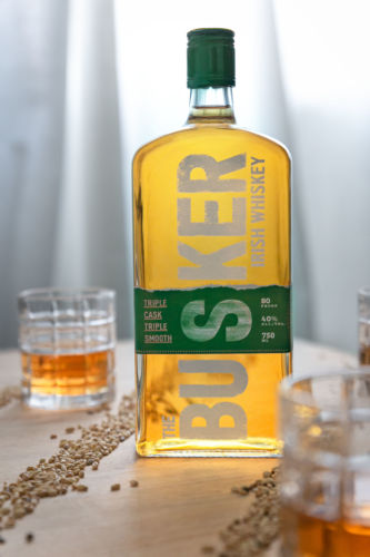 The Busker Whiskey photographed with a two clear glasses and seeds lined up diagonally on a with a wooden background.