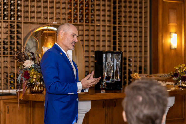 A man in a blue suit talking in front of the guests.