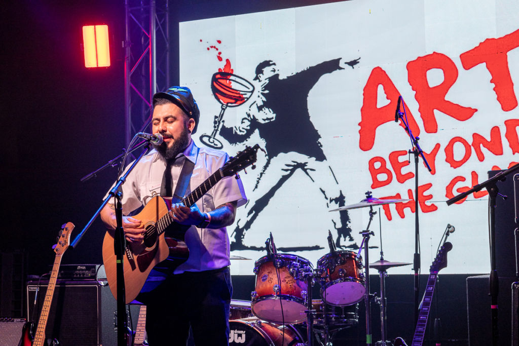 A musician singing while playing a guitar during the Art Beyond the Glass 2022.