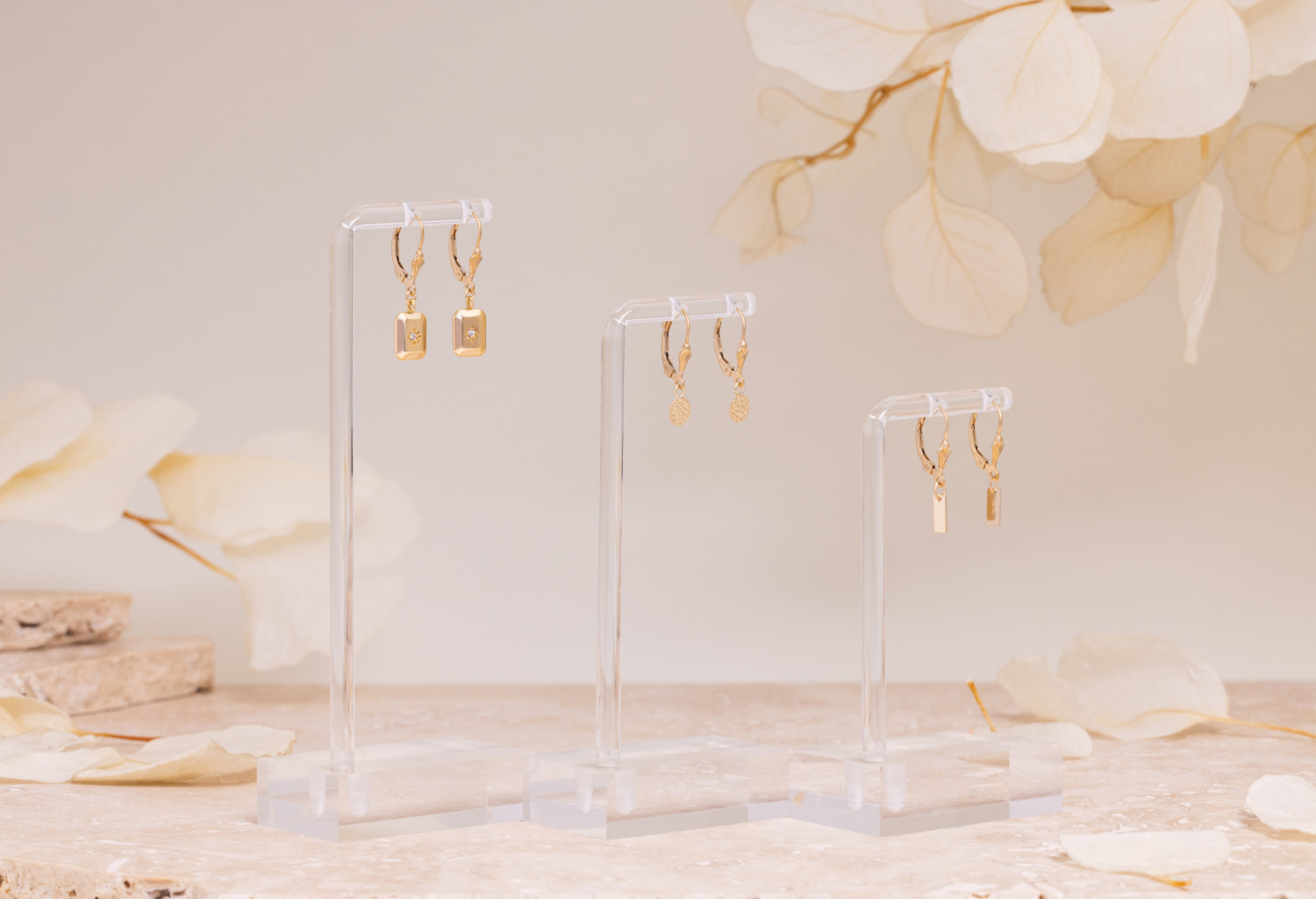Gold earrings on a cream marble surface.