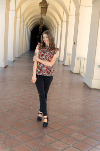 A woman with a multicolored shirt and black pants posing in an empty hallway.