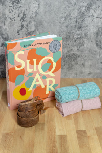 A book entitled Suqar with wooden cups and two towels in lilac and turquoise.