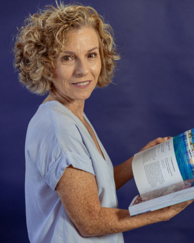 A blonde woman in blue holding an open book.