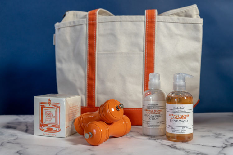 A large canvas tote with orange linings photographed with Orange flower Chamomile hand wash and lotion bottles, orange pepper crushers, and a box of Orange flower and Chamomile candle.