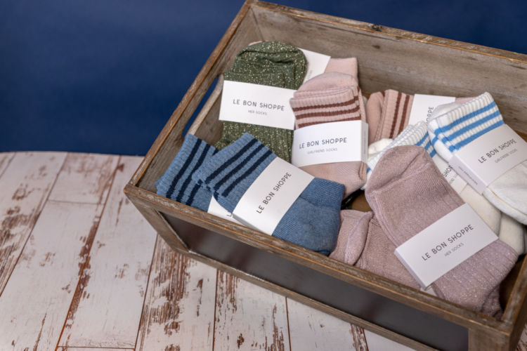 Various socks with the tag Le Bon Shoppe in a wooden box.