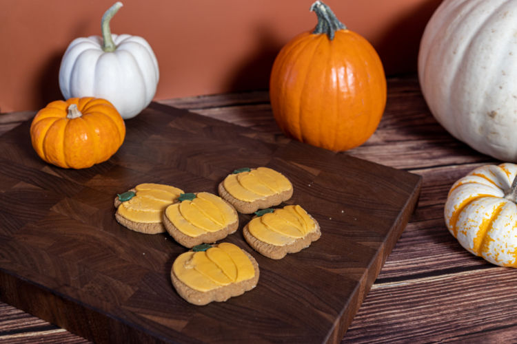 Pumpkin cookies on a wooden board photographed with pumpkins of different colors and sizes.
