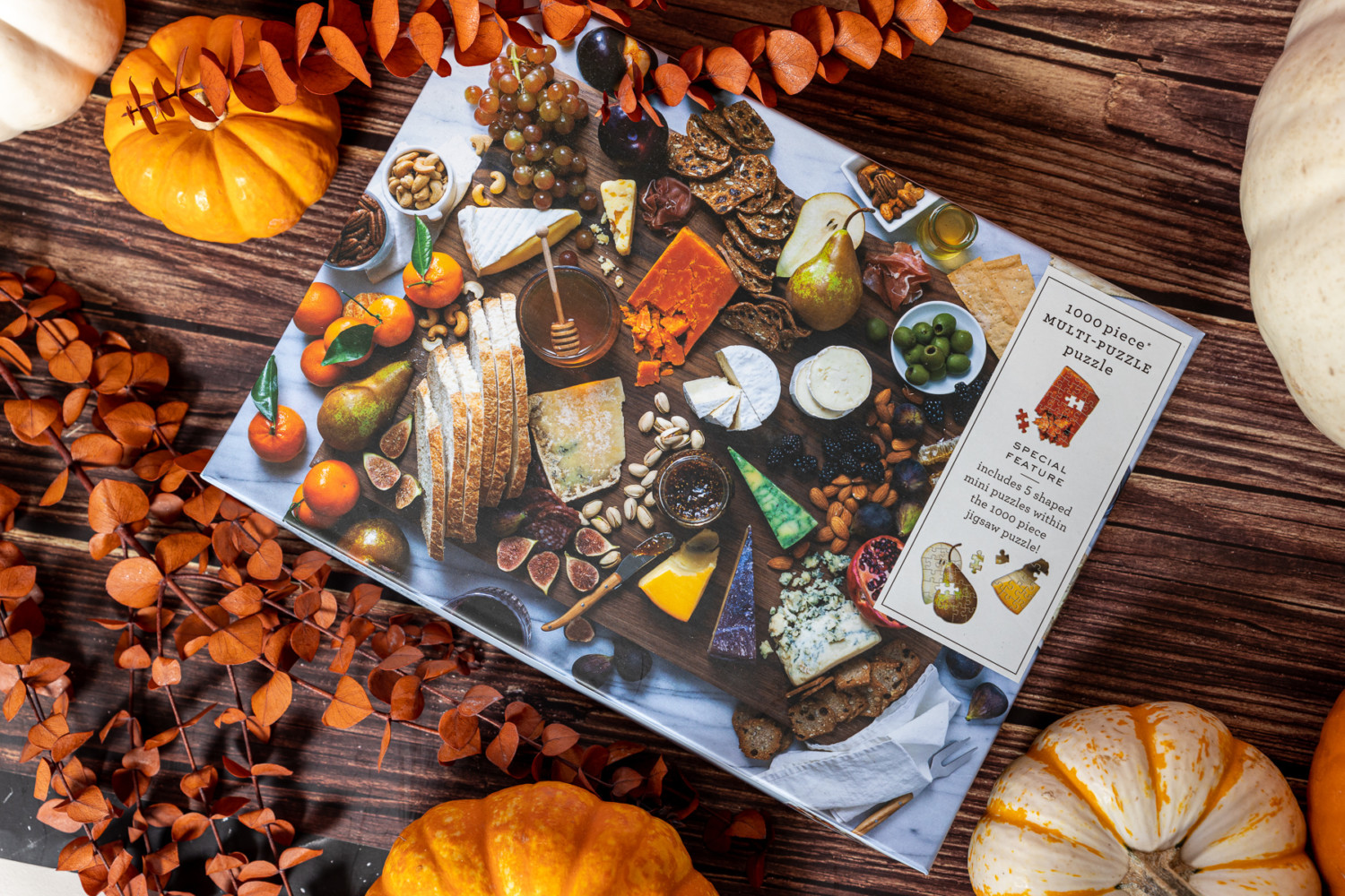 A 1000 piece puzzle box that featurers a charcuterie board photo, decorated with orange leaves and pumpkins with various sizes.
