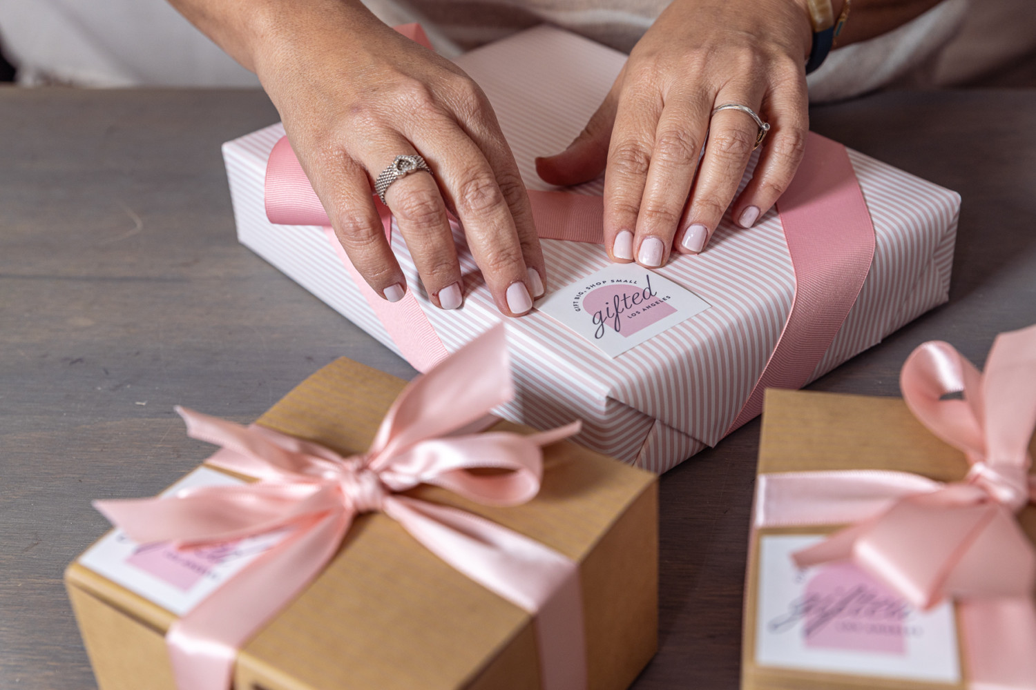 Hands preparing pink gift boxes with paper cards for the Gifted LA September shoot.