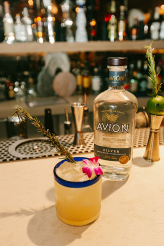 A bottle of Avion and a drink with a flower and a decorative herb.