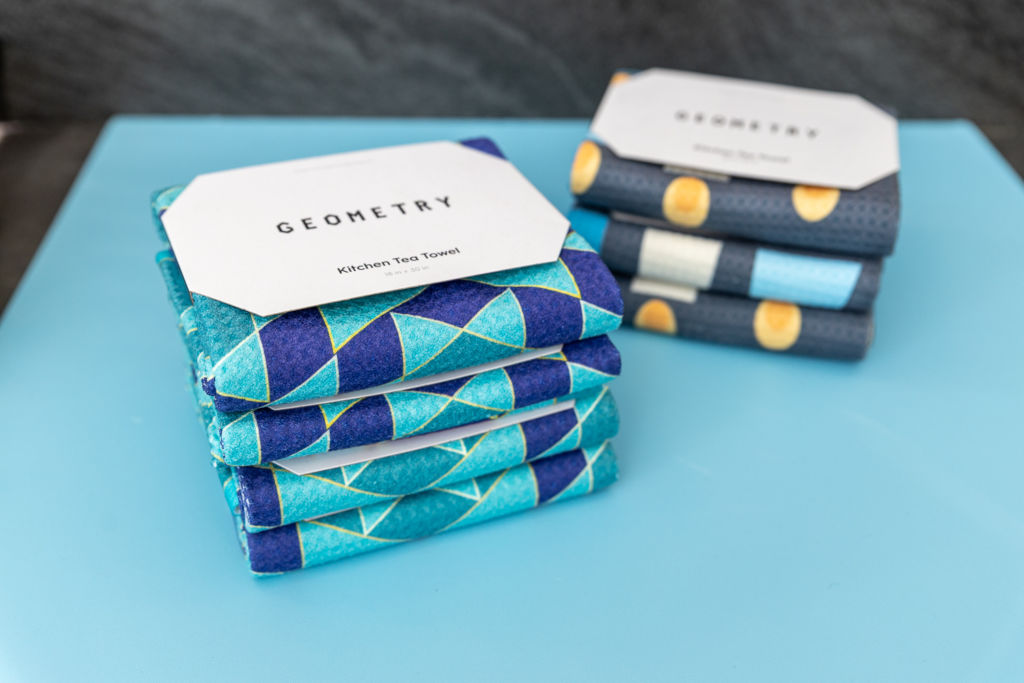 Two stacks of Geometry kitchen tea towel on a blue surface.