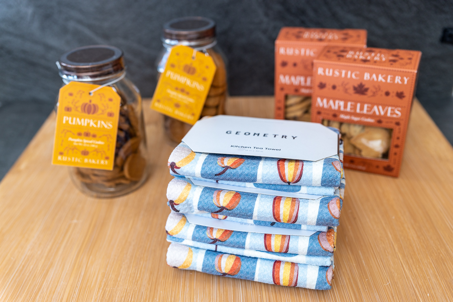 Pumpkin cookies, maple leave cookies, and a stack of Geometry kitchen towels on a table.