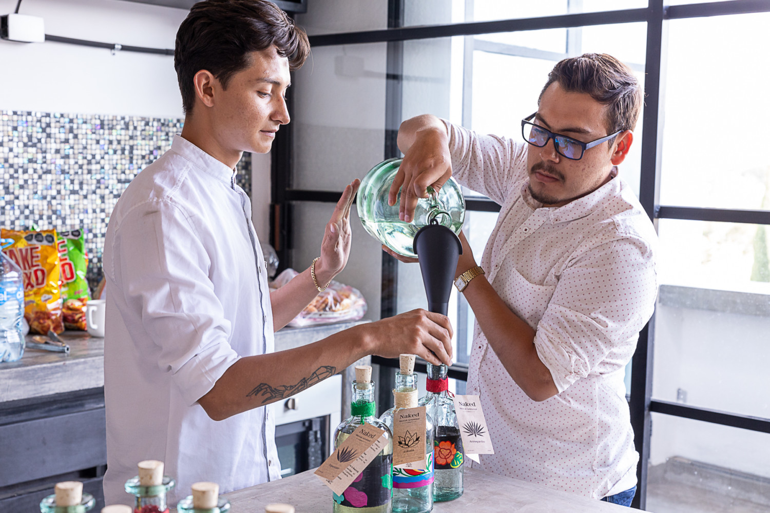 Two men in white shirts pour Naked Mezcal to other smaller bottles.