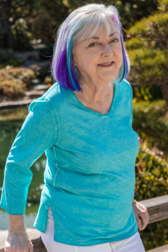 A woman in a blue, green, and white striped shirt poses for a camera with a pond as her background.